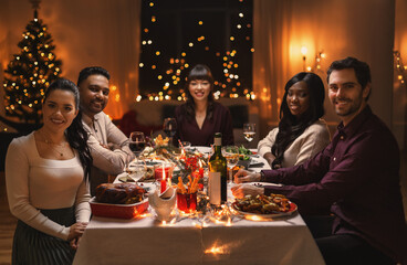 holidays, party and celebration concept - multiethnic group of happy friends having christmas dinner at home