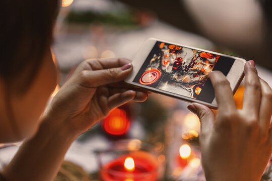 holidays, technology and celebration concept - hands with smartphone photographing served table decorations at christmas dinner