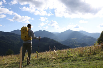 Tourist with backpack and trekking poles enjoying mountain landscape, back view. Space for text