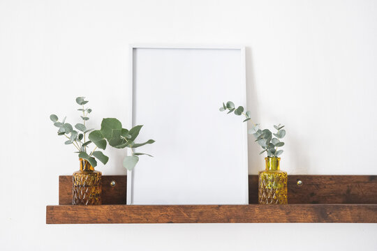 Image of mock up scene with white picture frame on brown shelf against white wall. Copy space