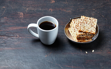 White cup with coffee and crunchy crispbread in a metal bowl on a wooden background, closeup. Tasty breakfast, morning routine concept