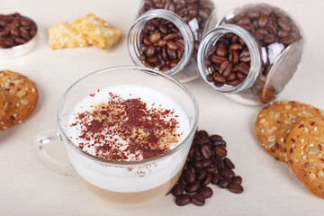 Cup of cappuccino with chocolate crumbs, cookies, crackers and coffee beans on table.