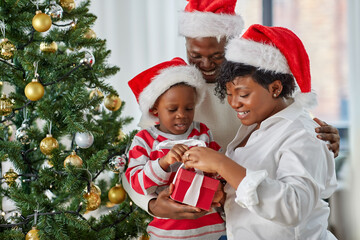 family, winter holidays and people concept - happy african american mother, father and little son opening gift box at home on christmas