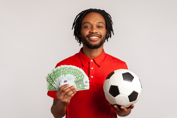 Attractive guy with toothy smile wearing red casual style T-shirt, holding soccer ball and euro...