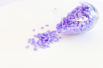 capsules of purple wax for depilation in a transparent glass, on a white background