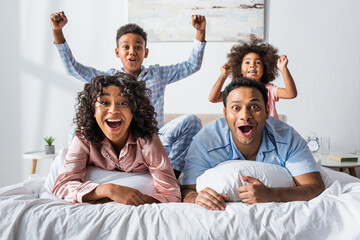 excited african american couple looking at camera near kids showing yeah gesture in bedroom