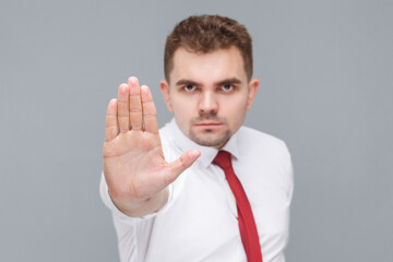 Stop it. Portrait of young handsome serious man in white shirt and tie standing with stop hand and looking at camera with serious face. indoor isolated on gray background.