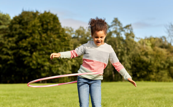 childhood, leisure and people concept - happy african american girl playing with hula hoop at park