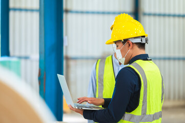 Team engineers and foreman wear a mask, hard hat, and vest. Standing consult discuss industrial production management. Explaining job details through laptops and tablets in factories or warehouses.