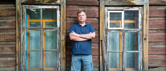 Fototapeta na wymiar An adult man stands at a wooden abandoned building.