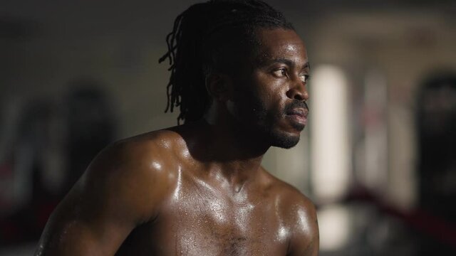 Portrait of perspiring African American confident man sitting in gym breathing. Endurant strong handsome sportsman resting working out indoors. Masculinity and healthy lifestyle concept