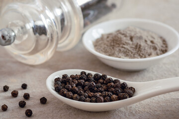 Black pepper corn on spoon and black pepper powder in bowl.