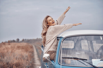Beautiful young woman keeping arms outstretched and looking happy while enjoying road trip in minivan