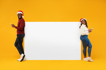 Black Couple Using Smartphones Near Poster For Christmas Advertisement, Studio