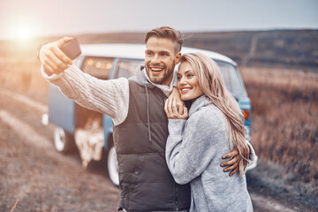 Beautiful young loving couple embracing and making selfie while spending time near their retro minivan