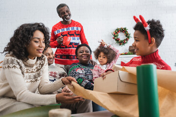 mother and son packing gift box near happy african american family
