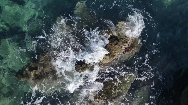 Drone view on turquoise sea water, waves, splashes, foam and rocks.