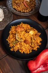 Delicious plate of Valencian paella with chicken and vegetables on a brown table with paprika and saffron
