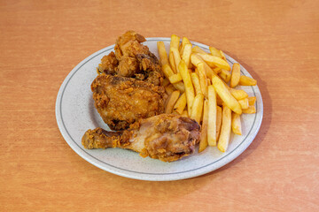 Portion of broaster chicken in batter fried in olive oil garnished with French fries on wooden table