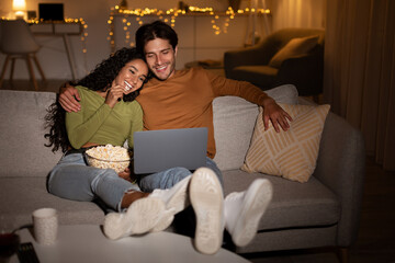 Naklejka premium Young Spouses Watching Film On Laptop Relaxing At Home