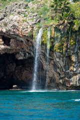 Fototapeta na wymiar Freshwater waterfall falling on the shores of the Mediterranean between caves and cliffs
