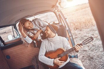 Handsome young man playing guitar for his girlfriend while spending time in motor home