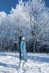 Fototapeta na wymiar Young woman is resting in the winter forest. Blue coat on a background of white snow