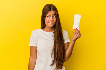 Young caucasian woman holding a compress isolated on yellow background confused, feels doubtful and unsure.