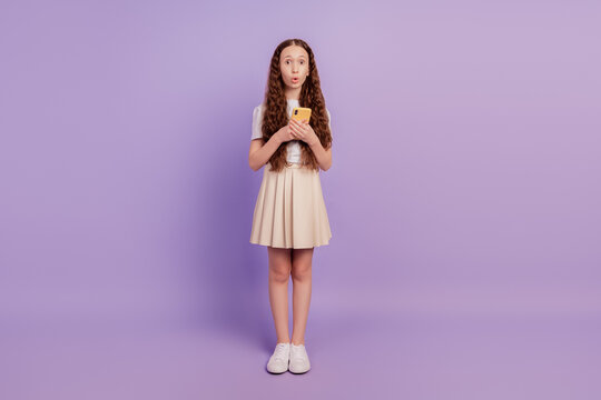 Portrait of excited crazy shocked small girl hold phone omg reaction open mouth on purple background