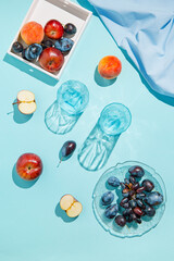 Creative composition made of plate with fruits, glasses, apples on pastel blue sunlit background with cloth and shadows. Summer and refreshment concept. Harvest theme. Top view. Flat lay