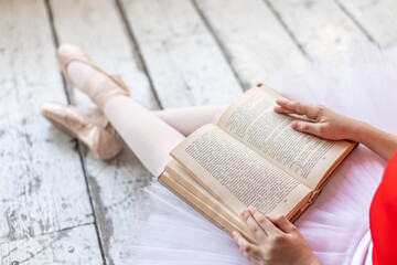 Ballerina in ballet pointe shoes sitting in red leotard and reading a book