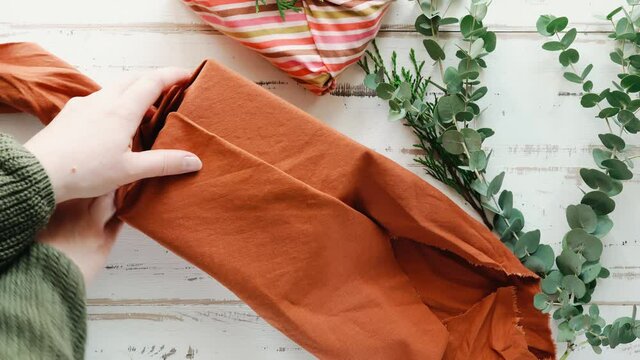 Furoshiki tissue wrapping of presents. Female hand wrapping a gift in eco friendly reusable fabric package. Top view. Presents packed in plastic free. Zero waste lifestyle. 4K UHD