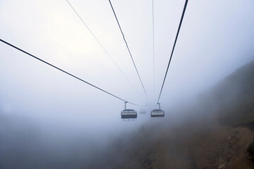 Cable car in the mountains with clouds or fog. View from the cable car to the mountain landscape....