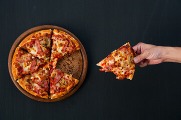 Hand holding pizza on a wooden board and black backdrop