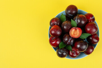 Blue bowl with plums on yellow background
