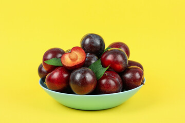 Blue bowl with plums on yellow background
