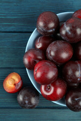 Blue bowl with plums on a blue wooden table