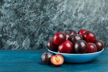 Blue bowl with plums on a blue wooden table
