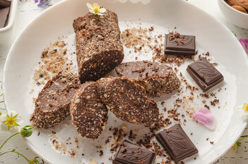 Vegetarian chocolate sausage made from nuts, cocoa, cookies on a white plate
