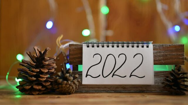 Notebook with the inscription 2022 in Christmas decorations and multicolored garland lights. Concept for the coming 2022. Selective focus on lettering.
