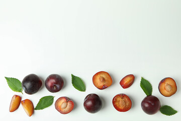 Tasty plums with leaves on white background