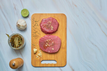 Fresh raw tuna steaks on wooden cutting board on marble table. Top view.