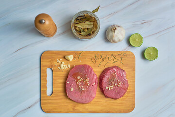 Fresh raw tuna steaks on wooden cutting board on marble table. Top view.