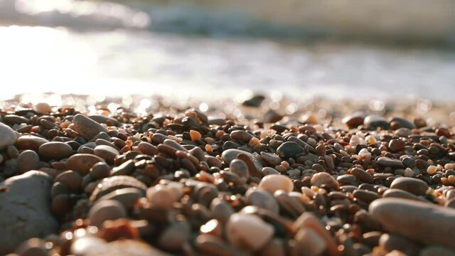 4k video. Waves on the beach with pebbles at sunset, the sun goes into the water. The concept of feeling calm and zen 