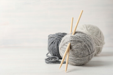 Balls of yarn with knitting needles on white wooden background
