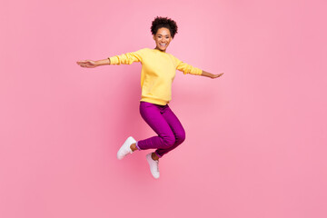 Photo of pretty childish lady wear yellow pullover jumping high arms sides smiling isolated pink color background