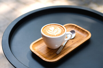 A white cup of cappuccino with latte art on the wooden tray in cafe. Close-up.