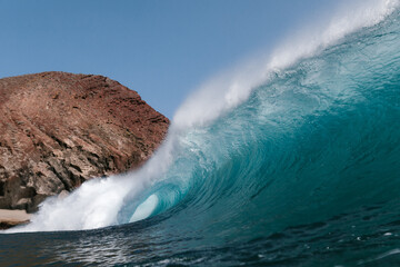 Naklejka premium Blue wave breaking front a red mountain in Tenerife