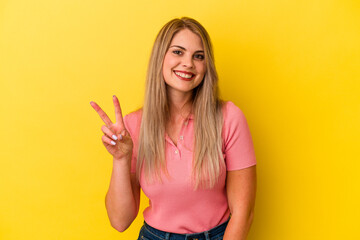 Young russian woman isolated on yellow background showing victory sign and smiling broadly.