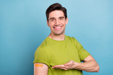 Photo of optimistic young brunet guy point plaster wear green t-shirt isolated on blue color background